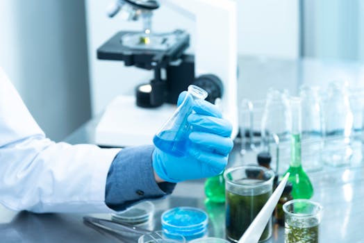 pexels-photo-2280571-2280571 Scientist in gloves analyzing blue liquid in a laboratory setting with microscope and glassware.